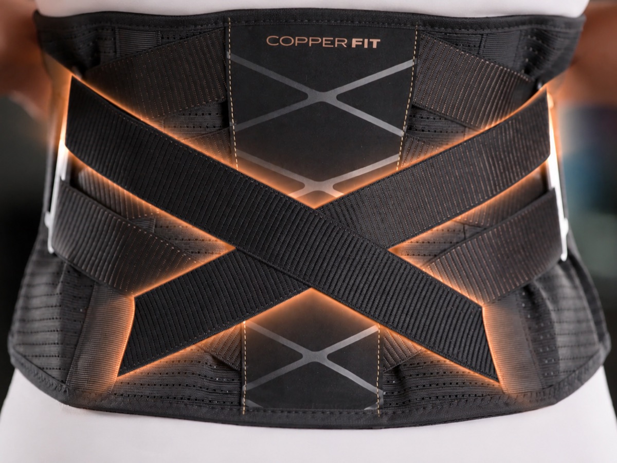 Copper Fit X Back adjustable back brace worn at the waist, its crossed support straps lit with a copper glow